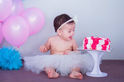 Baby in tutu sitting next to a large pink frosted cake for professional baby photography Glasgow